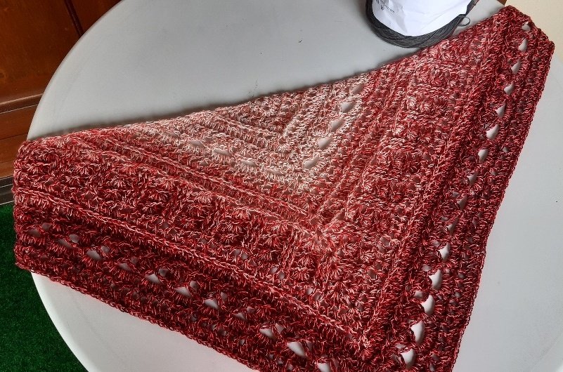 Triangle crocheted shawl in variegated red and copper yarn laid flat showing lace rows and border