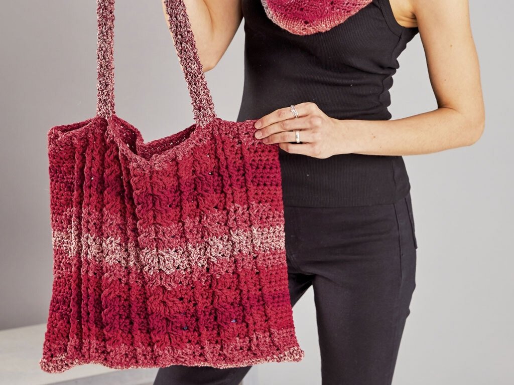 Gehäkelte Shopper‑Tasche in Rot‑Rosa mit Reliefmaschen, getragen von einer Person