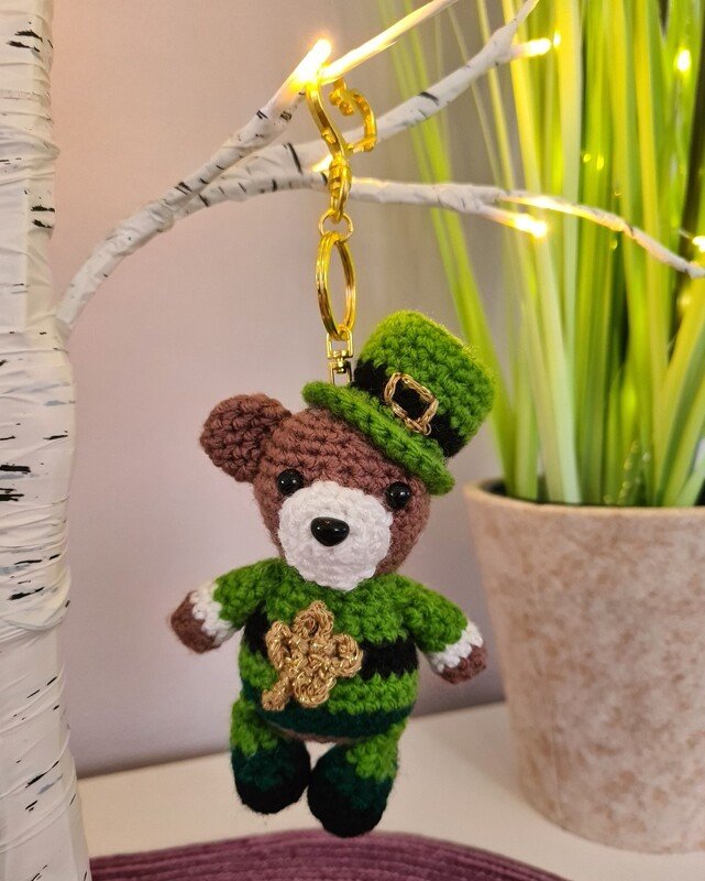 Gehäkelter Amigurumi-Teddybär als Schlüsselanhänger mit grünem Zylinderhut, Kleeblatt und grün-schwarzem Outfit.