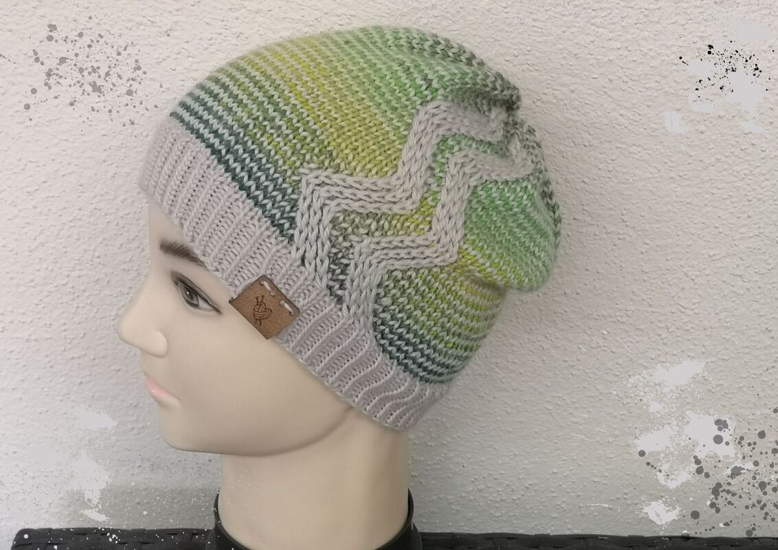 Gestrickte Beanie in Grün- und Grautönen mit Zickzack-Muster auf einem Schaufensterkopf