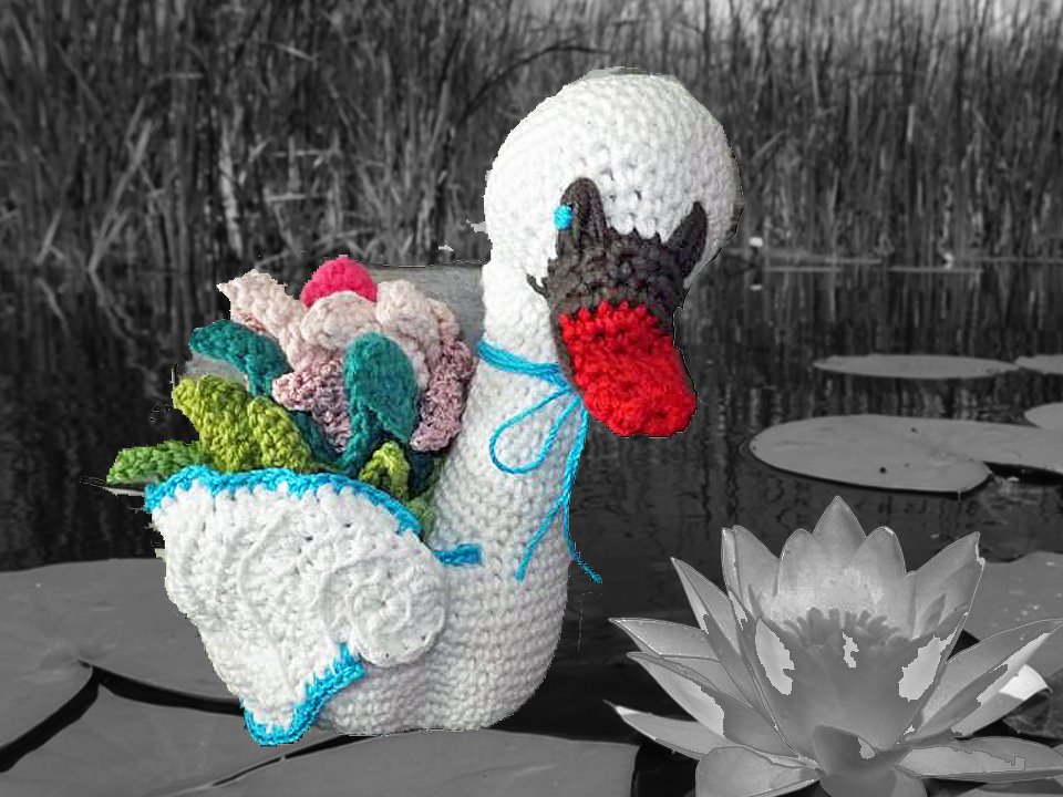 Weiß gehäkelter Schwan-Korb mit rotem Schnabel, blauem Rand und bunten Häkelblumen auf Seerosenblatt