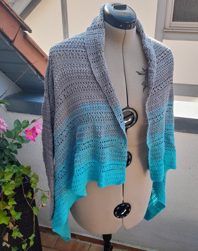 Offene gehäkelte Jacke in Grau und Türkis auf einer Schneiderpuppe mit Ombré‑Verlauf