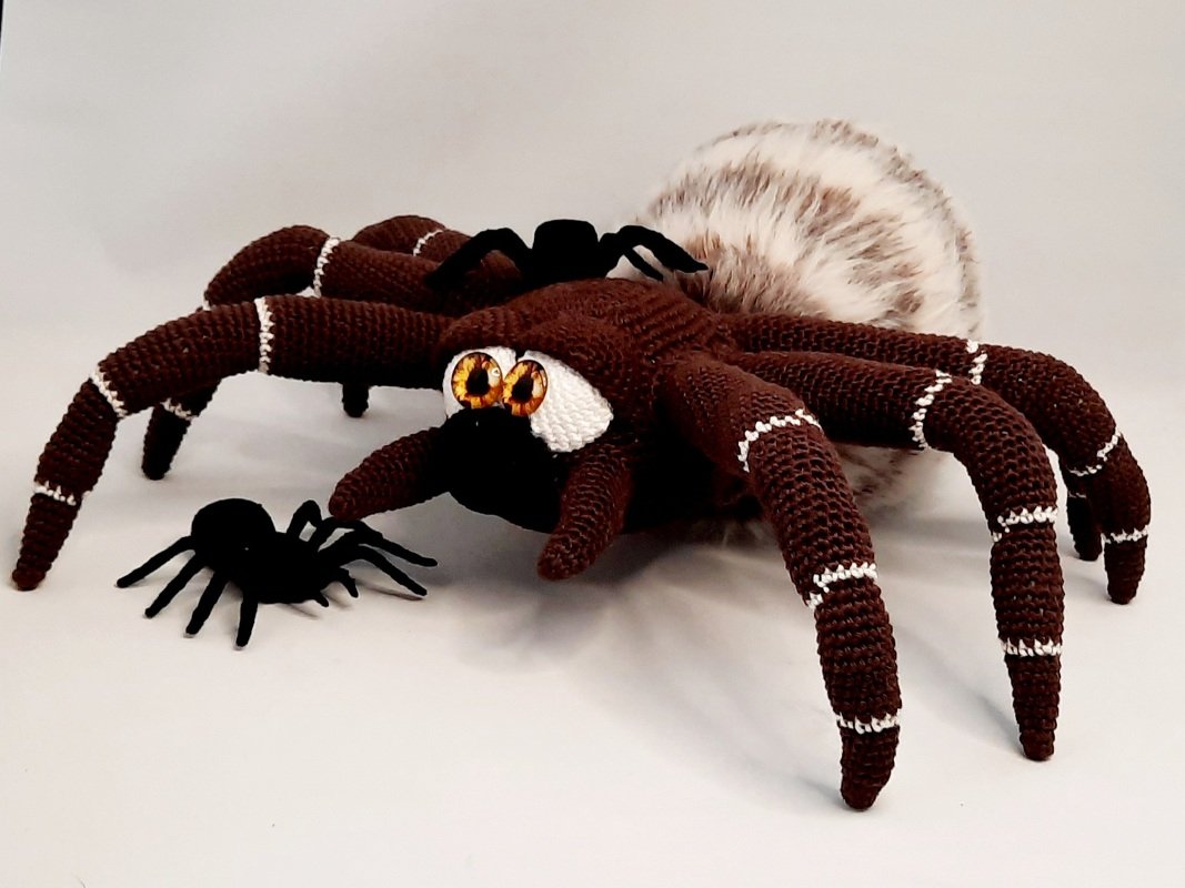 Close-up of a crocheted tarantula amigurumi focusing on segmented banded legs, amber eyes and a textured fuzzy abdomen