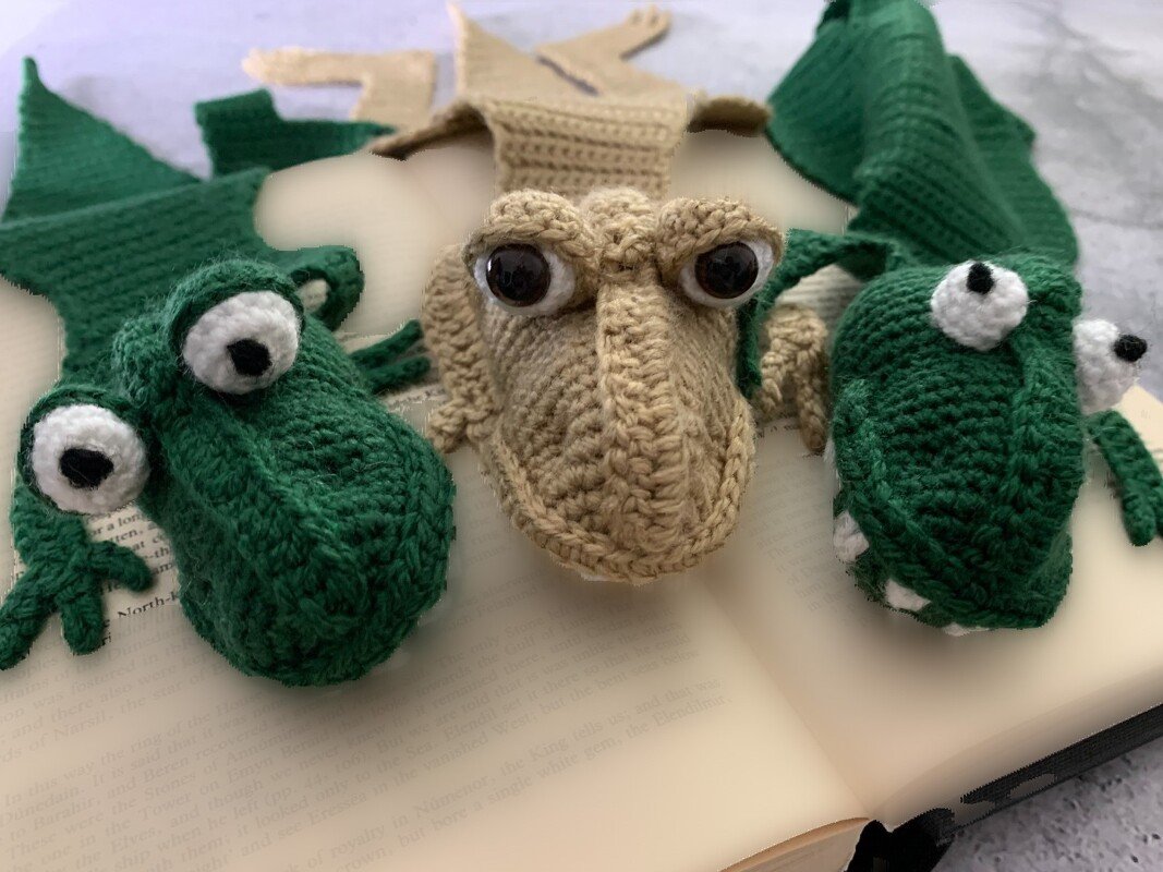 Three crocheted crocodile head bookmarks, two green and one beige, with eye details on an open book