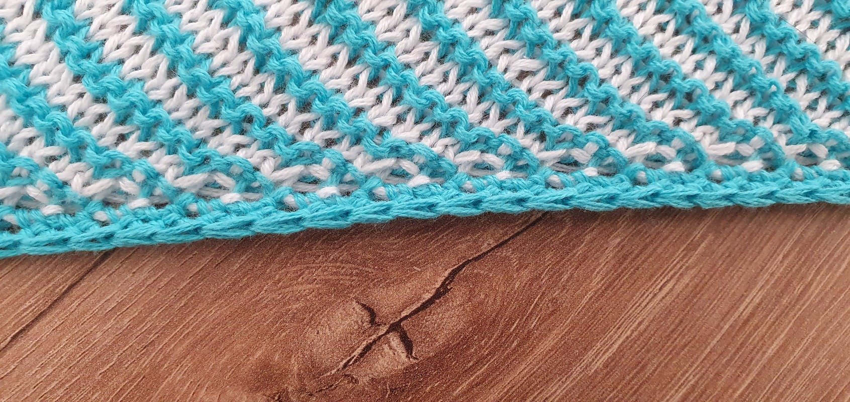 Close-up of a knitted shawl in turquoise and white with a geometric stitch motif and a solid turquoise edge.