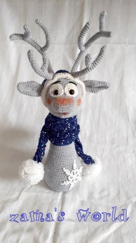 Gehäkeltes graues Rentier-Amigurumi mit verzweigten Geweihen, dunkelblauem Schal, Pompons und Schneeflocke