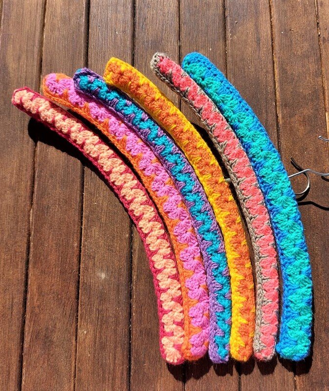 Sechs bunte gehäkelte Kleiderbügelbezüge im Muschelmuster auf Holz