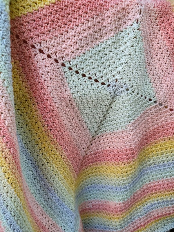 Nahaufnahme einer gehäkelten Babydecke in Pastellfarben mit zentralem Viereck und gestreiften Reihen