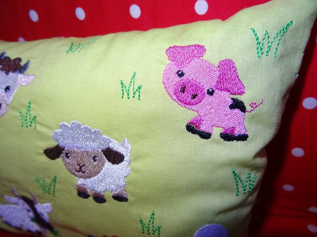 Rosa Schwein und weißes Schaf als Stickmotive auf hellgrünem Stoff