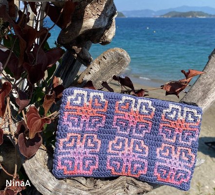 Gehäkelte Clutch in Blau, Rosa und Lila mit geometrischem Muster auf Treibholz am Strand