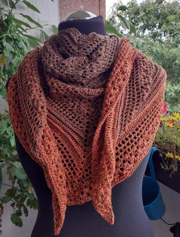 Nahaufnahme eines gehäkelten Dreieckstuchs mit Lochmuster und Farbverlauf in Rosttönen auf Schneiderpuppe