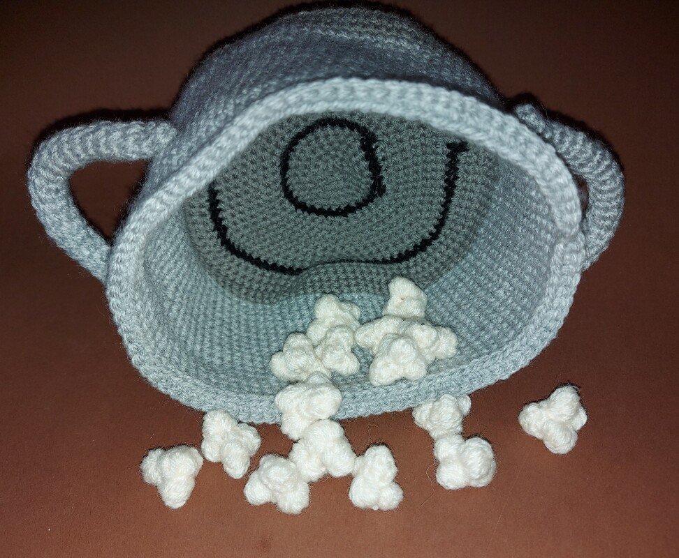 Gehäkelter hellblauer Popcorn-Eimer mit lächelndem Gesicht und weißen Popcorn-Stücken