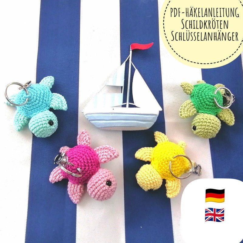 Four small, colorful crocheted turtle keychains in blue, pink, yellow, and green on a blue-and-white striped background beside a small sailboat decoration.