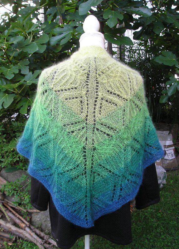 Gestricktes Dreieckstuch mit Farbverlauf von hellgrün zu blau und Blatt
Lochmuster auf einer Schaufensterpuppe vor grünem Laub.