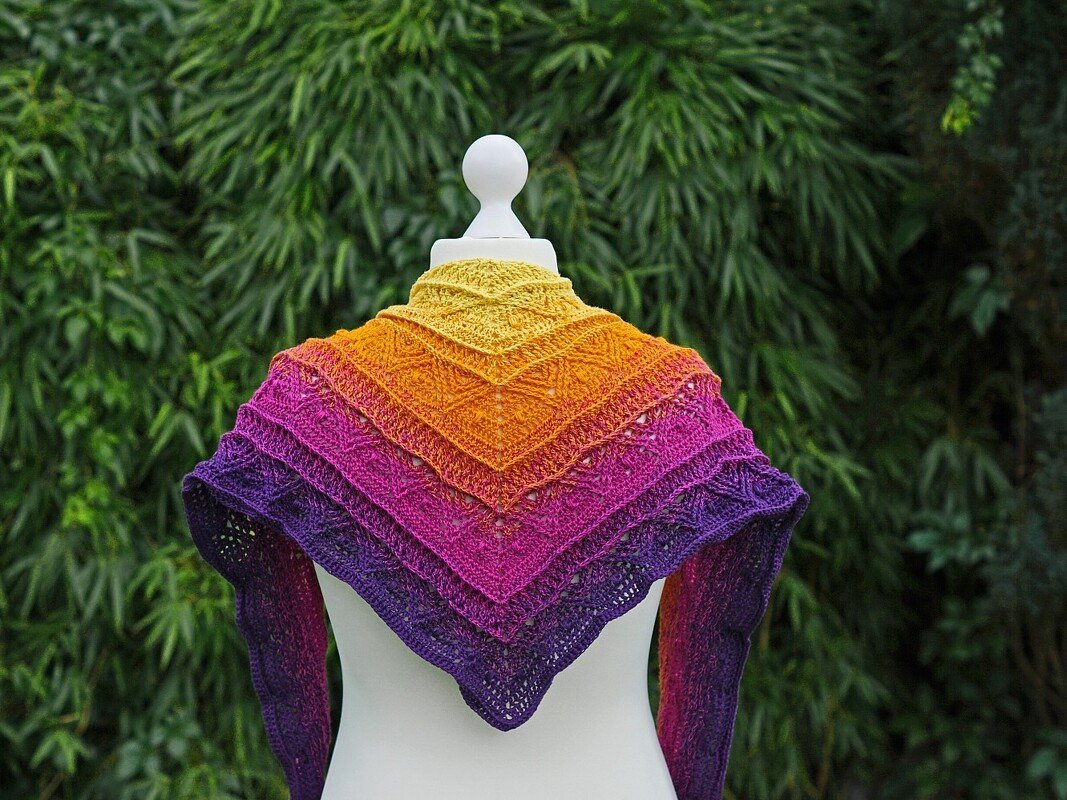 Gehäkeltes Dreieckstuch in Gelb‑Orange‑Pink‑Violett auf weißer Schaufensterpuppe vor grünem Hintergrund