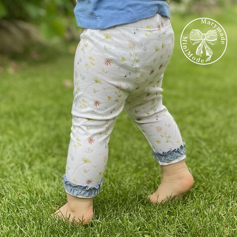 Nahaufnahme der Rückseite einer Babyhose mit floralem Muster und Rüschensaum, stehendes Kleinkind auf Gras