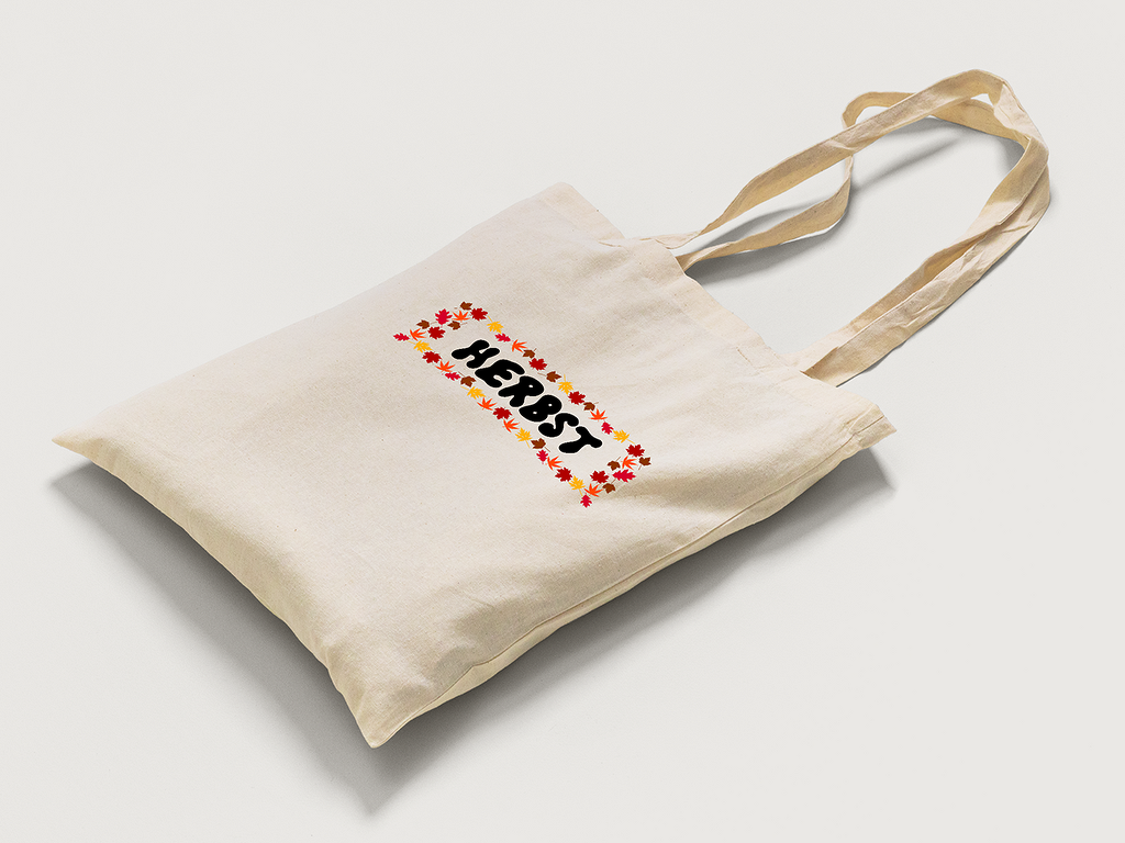 Beige Baumwolltasche mit schwarzem Schriftzug 'HERBST' in einem rechteckigen Rahmen aus roten, orangen und gelben Herbstblättern