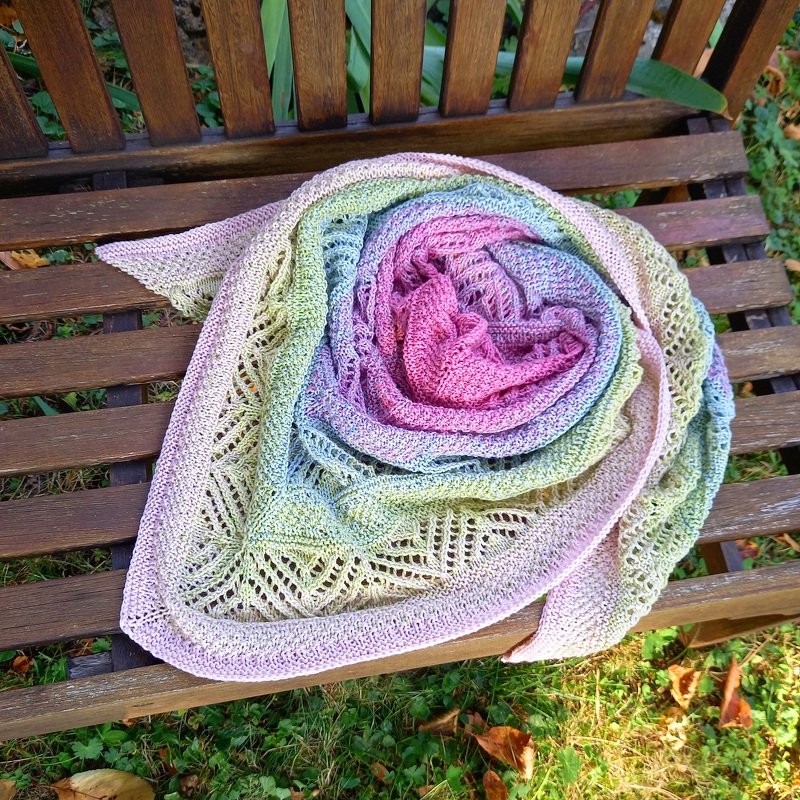 Gestricktes Dreieckstuch mit pastellfarbenem Farbverlauf und Ajourrand auf einer Holzbank