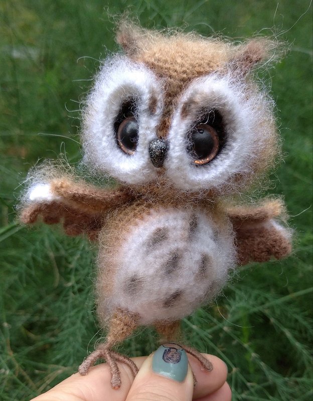 kleine gehäkelte braune Amigurumi-Eule mit großen Augen, gehalten an den Krallen