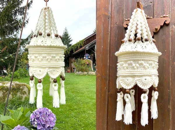 Cremefarbene, gehäkelte Hängedekoration mit aufwendigen Mustern, Holzperlen und langen Quasten vor Holzwand und Garten