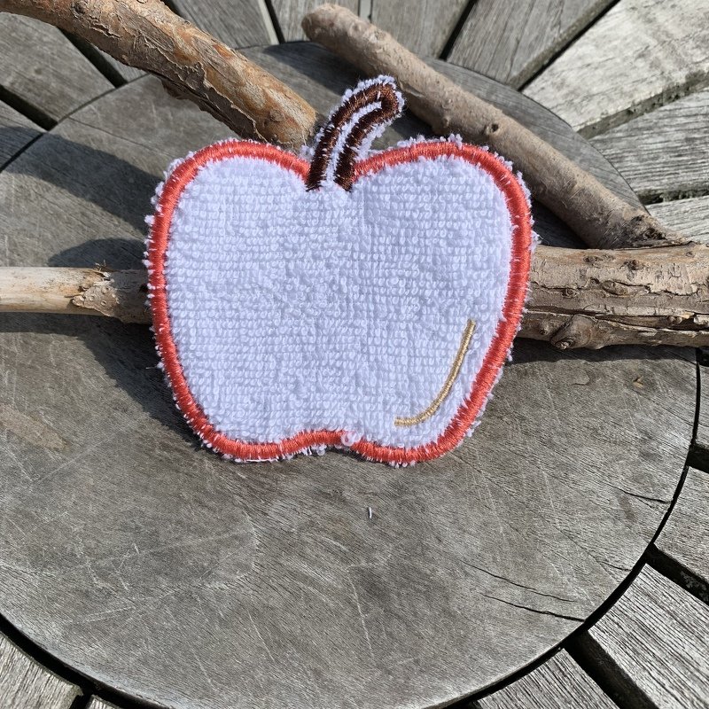 Weiße Apfel-Applikation aus Frottee mit orangem Rand und braunem Stiel auf Holzuntergrund