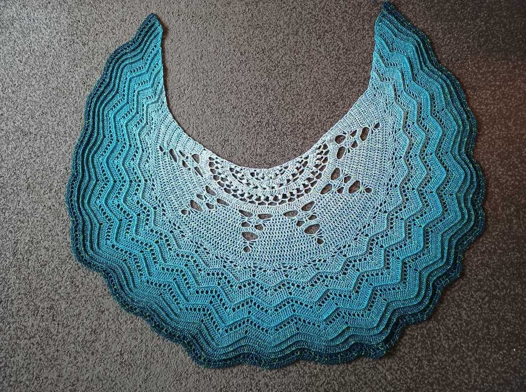 Crescent crochet shawl in blue-to-teal gradient with central lace panels, chevron waves and scalloped edge laid flat