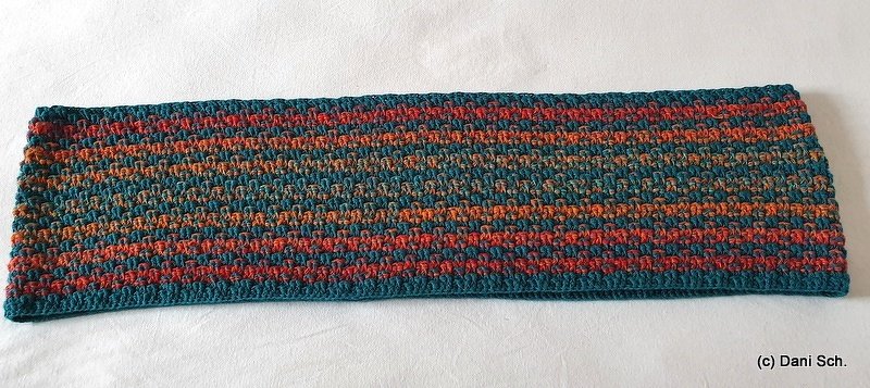 Striped crocheted loop scarf laid flat showing textured horizontal bands in teal, orange, and red.