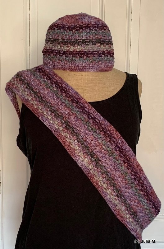 Variegated crocheted hat and loop scarf on a dress form in purple, green, and gray yarn.