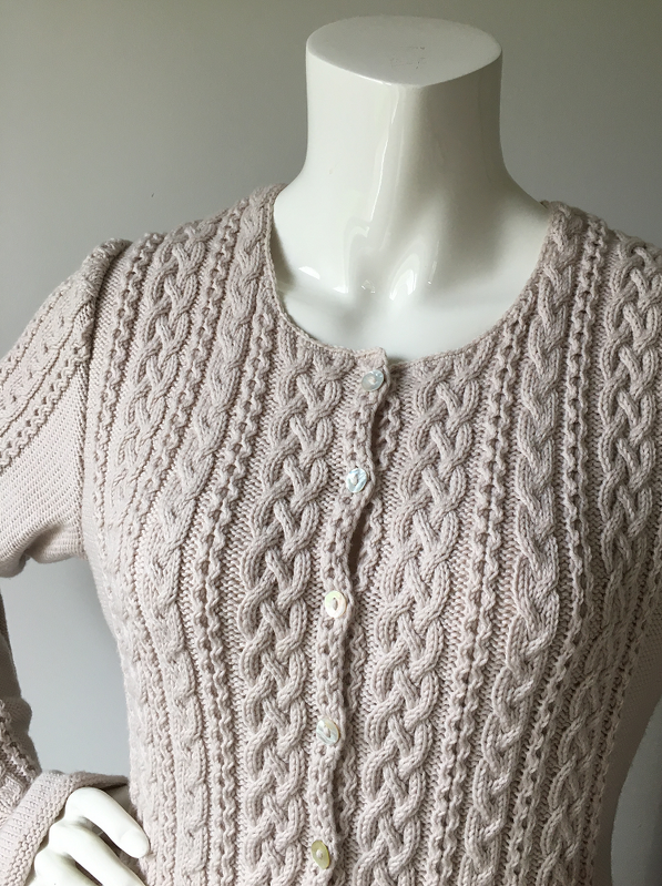Mannequin wearing pale neutral cable-knit women's button-up cardigan with braided cables and crew neck