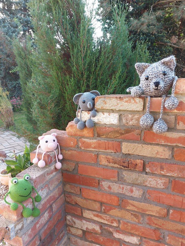 Vier gehäkelte Amigurumi (Koala, Frosch, Schwein, Kätzchen) auf einer Ziegelmauer