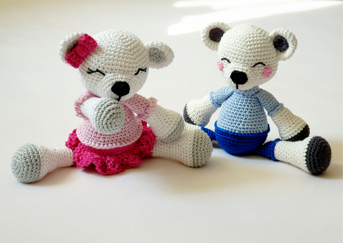 Zwei sitzende gehäkelte Amigurumi-Teddybären, einer rosa mit Schleife, einer blau mit Pullover