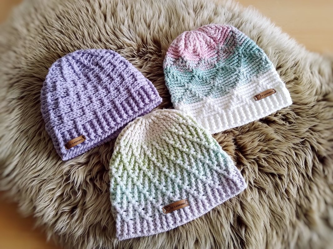 Drei gehäkelte Beanies in Pastelltönen mit unterschiedlichen Strukturmustern auf hellem Felluntergrund