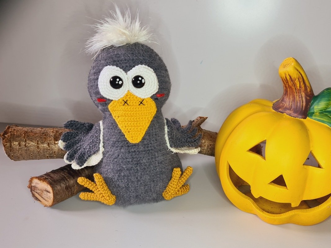 Handgehäkelter Vogel mit weißem Bommel neben herbstlicher Kürbisdekoration