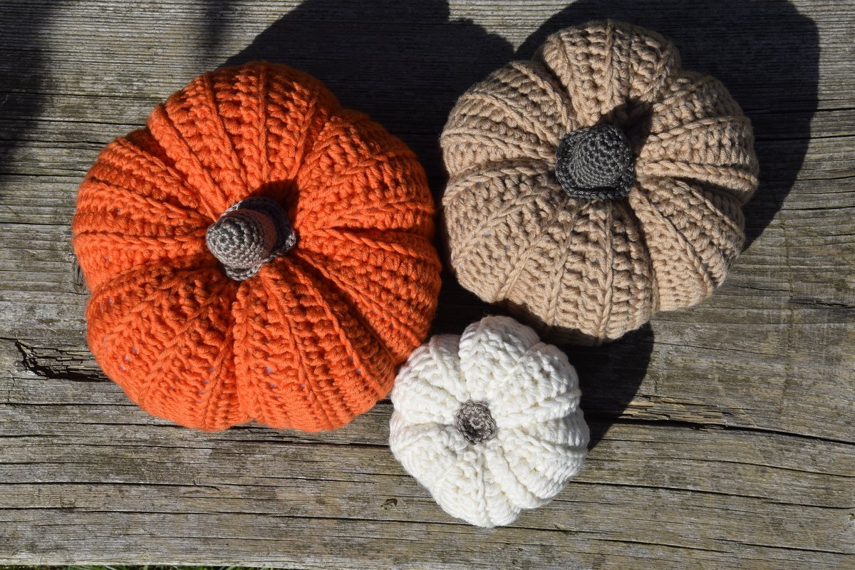 Kleine und große gehäkelte Kürbisse auf Holzbrett in orange, beige und weiß