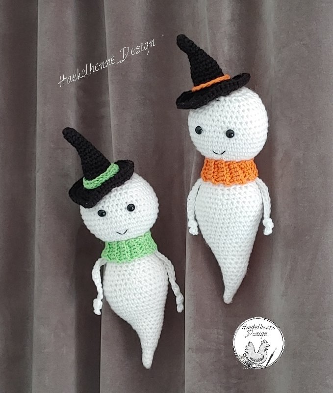 Zwei gehäkelte weiße Geister mit schwarzen Hexenhüten und grüner sowie orangener Halskrause