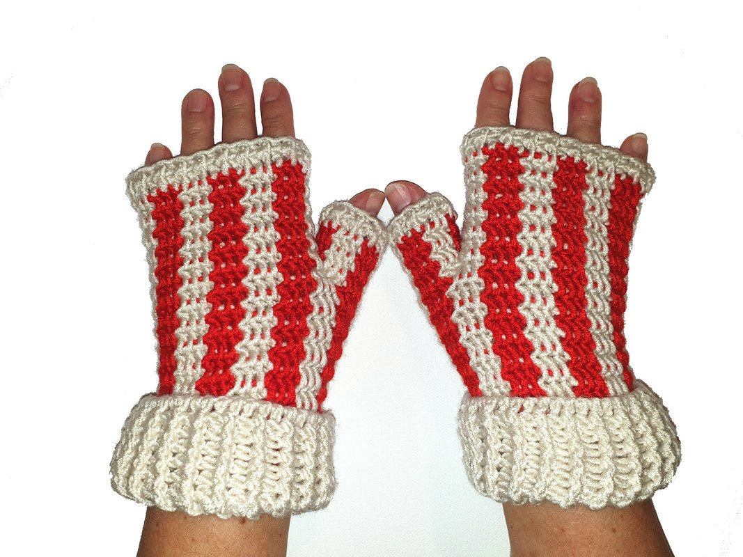 Zwei Hände mit rot-weiß gestreiften, gehäkelten fingerlosen Handschuhen auf weißem Hintergrund.