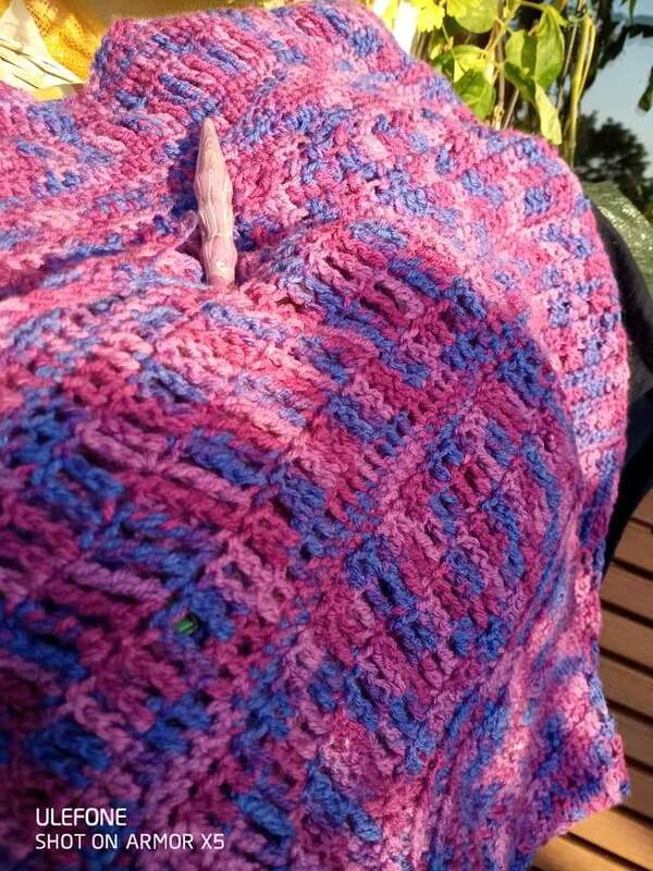 Nahaufnahme eines gehäkelten Schals in Pink und Blau mit Schalnadel