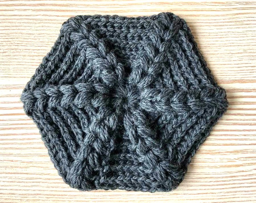 Dunkelgraues gehäkeltes Hexagon mit Reliefmuster auf Holzuntergrund