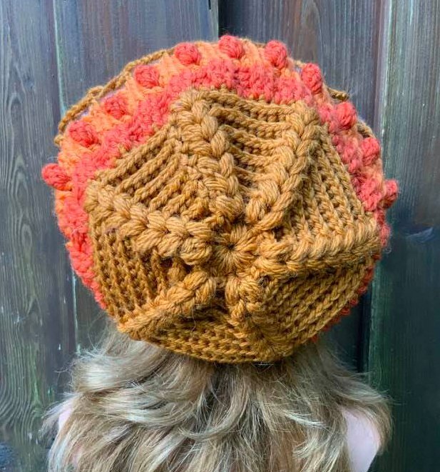 Rückansicht einer Person mit gehäkelter Mütze in Braun und Orange mit Noppen- und Zopfmustern.