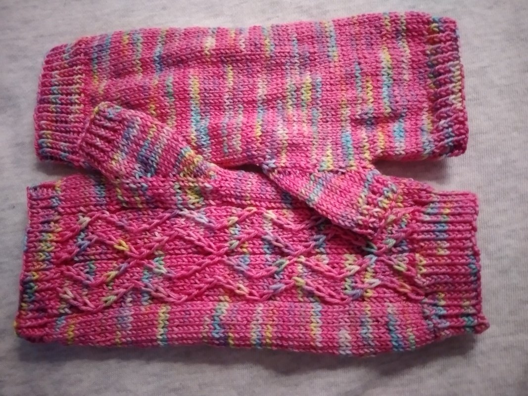 Zwei rosa mehrfarbige gestrickte Armstulpen mit Zopfmuster und Daumenöffnung auf hellem Untergrund