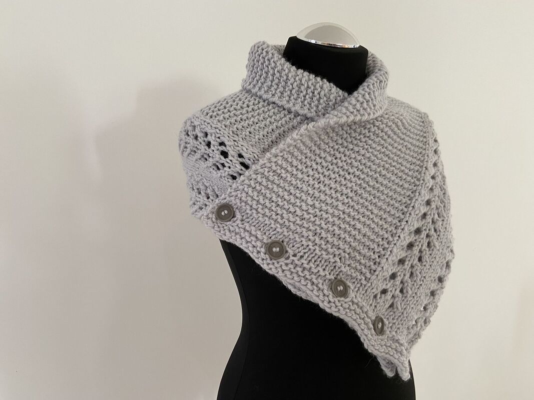 Grauer gestrickter Kragenschal mit hohem Kragen und mehreren Knöpfen auf schwarzer Schneiderpuppe