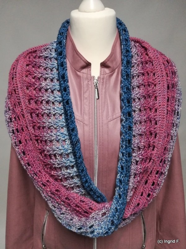 Crochet infinity cowl in pink-to-blue ombré with deep-blue trim displayed on a mannequin wearing a zip-front jacket