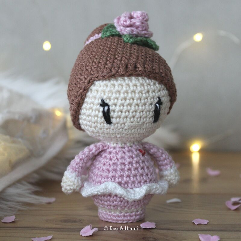 Gehäkelte Amigurumi-Ballerina in rosa Kleid mit Dutt und Rosenverzierung auf Holzuntergrund