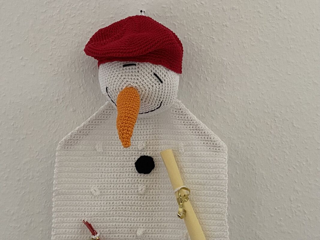 Gehäkelter weißer Schneemann-Wandbehang mit roter Mütze und orangefarbener Nase.