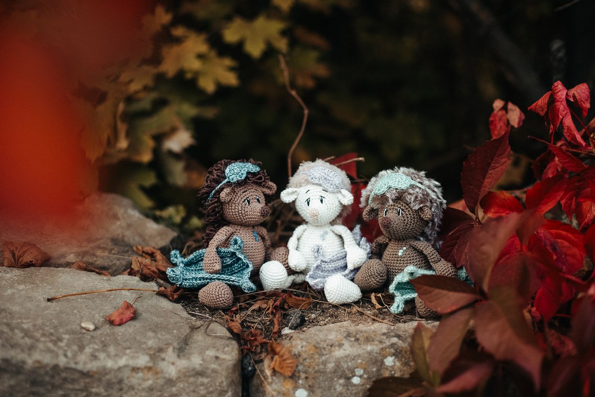 Drei gehäkelte Amigurumi-Tiere auf Steinen zwischen roten und gelben Herbstblättern.