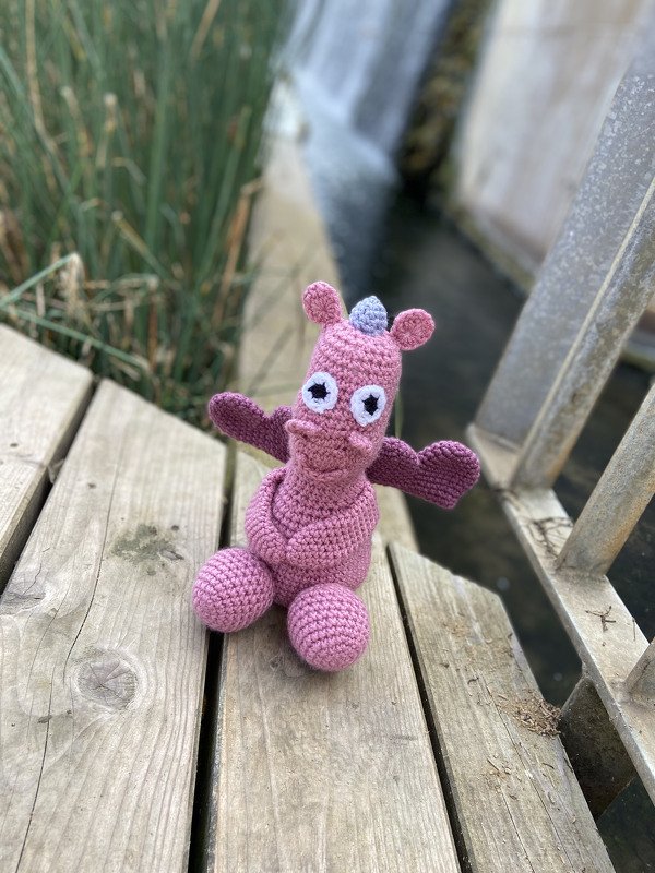 Sitzender Amigurumi-Drache in Rosa zeigt Beine, Flügel und Augen