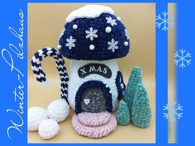 Nahaufnahme eines gehäkelten Amigurumi-Pilzhauses mit Schneeflockenapplikationen, gestreifter Zuckerstange und zwei gehäkelten Tannen