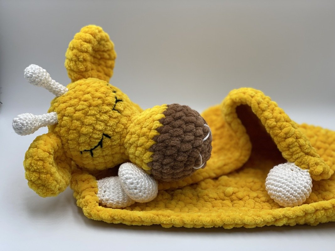 Yellow crocheted giraffe lovey with attached snuggle blanket on a neutral background