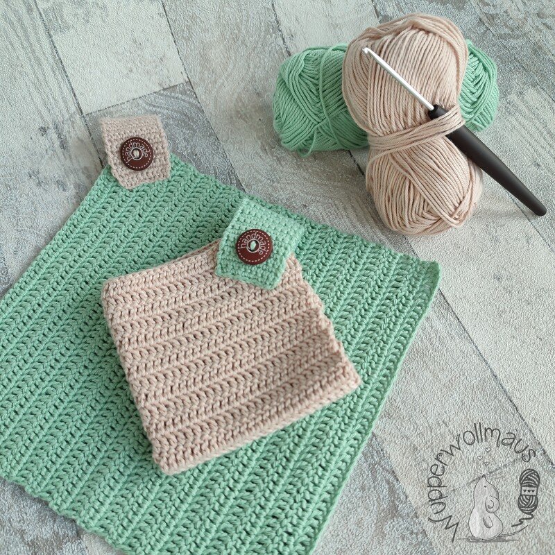 Gehäkeltes mintgrünes Deckchen und beiges Täschchen mit Knöpfen, Wollknäuel und Häkelnadel auf hellem Holzgrund