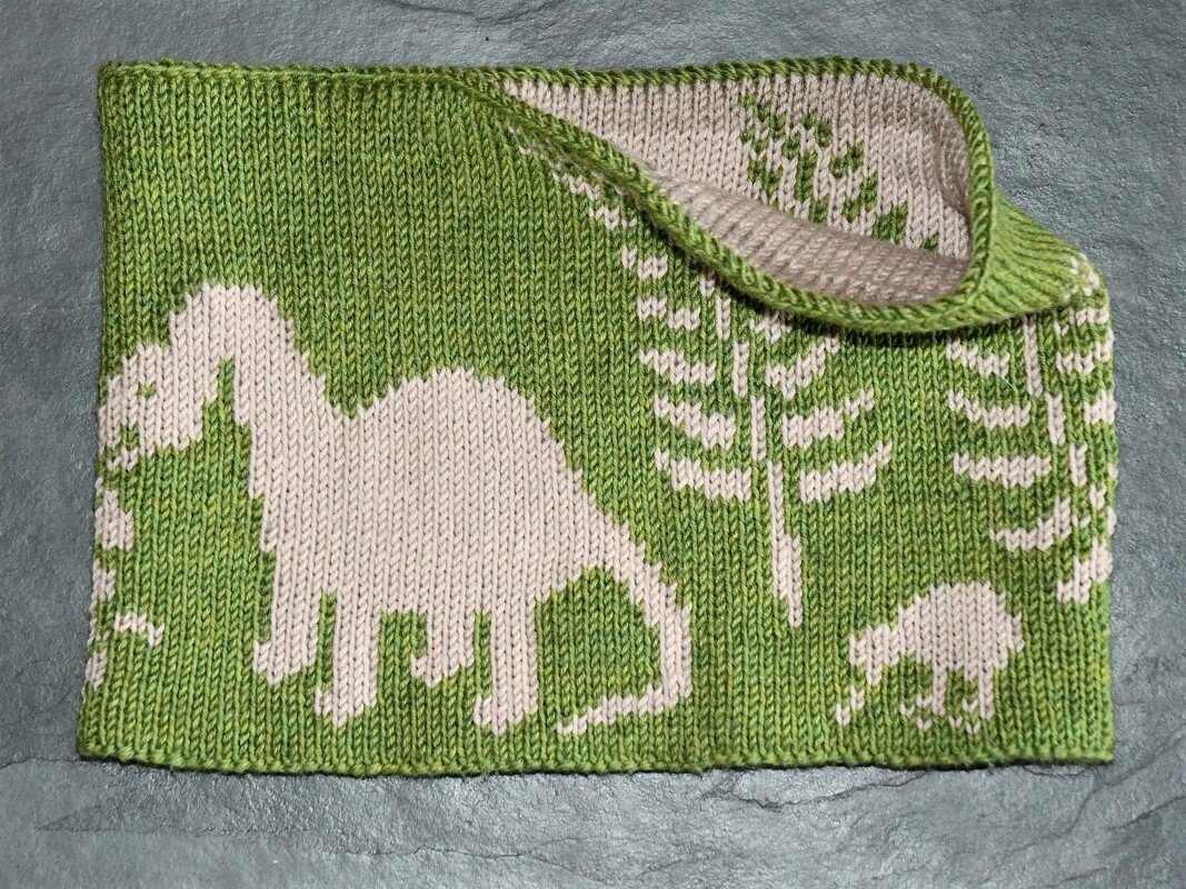Gestrickter Kinderloop in Grün und Beige mit Dinosaurier- und Pflanzenmustern, flach gefaltet